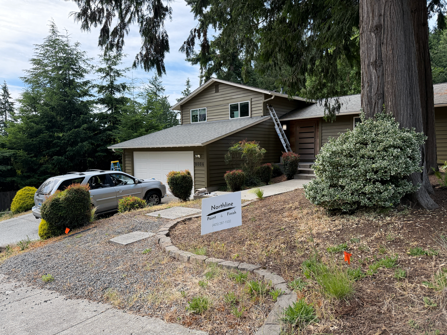Finished olive-green exterior repaint viewed from the street with a Northline Paint & Finish yard sign in the yard