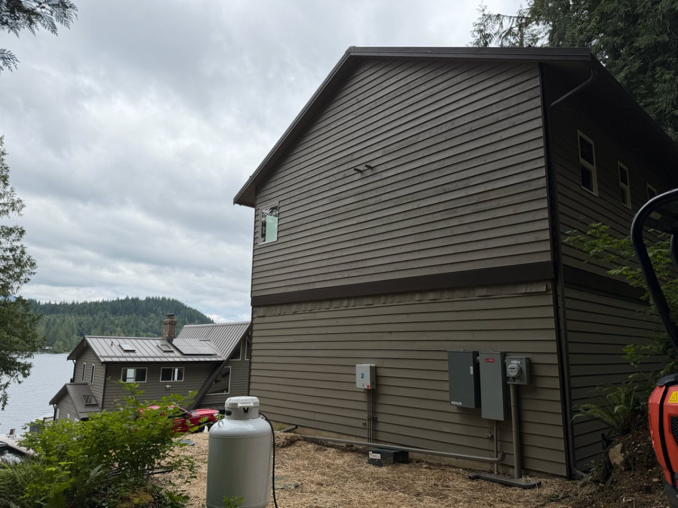Front gable of the finished lakefront custom home with dark exterior siding and the lake beyond