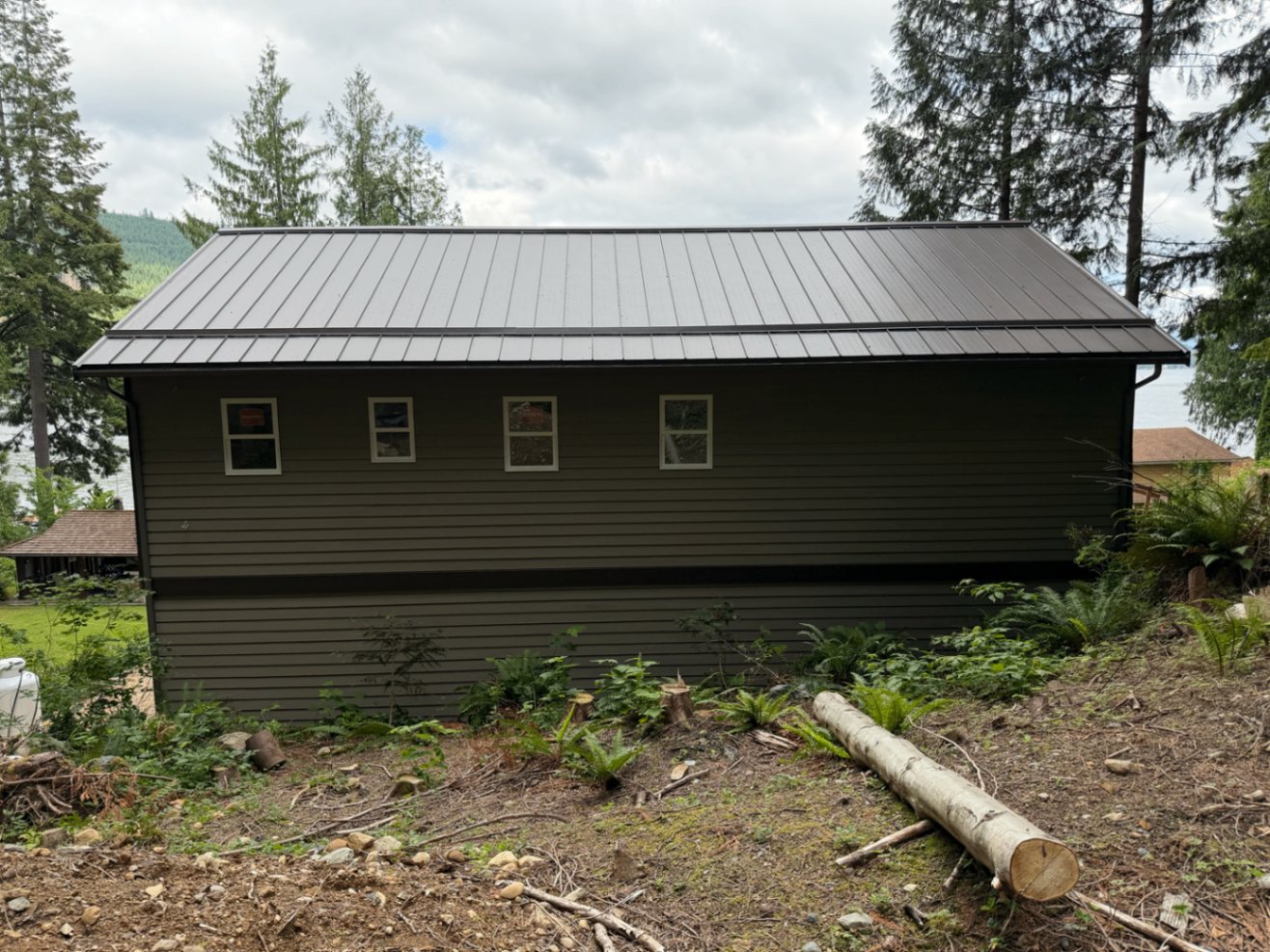 Finished lakefront home elevation in deep olive with a dark metal roof and the lake in the background